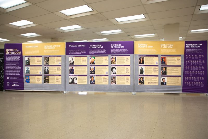 The Color of Freedom exhibit, consisting of three purple and gold walls displaying photos and descriptions of diverse military women.